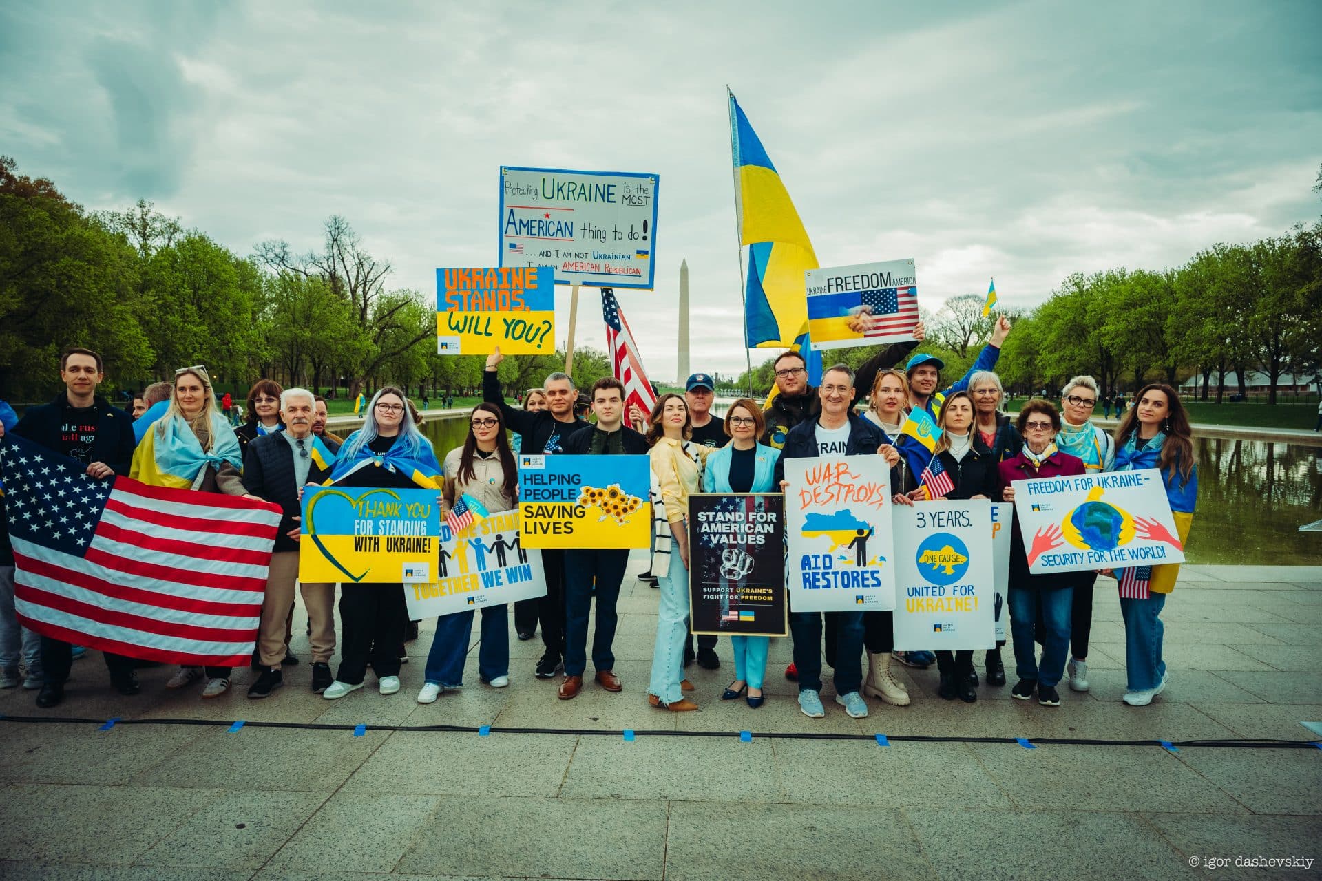 Standing with Ukraine rally in Washington, DC: a group of 20+ people with banners with words of support to Ukrainian people protecting their territories and freedom. Ukrainian and American flags in front of the people and on their shoulders.