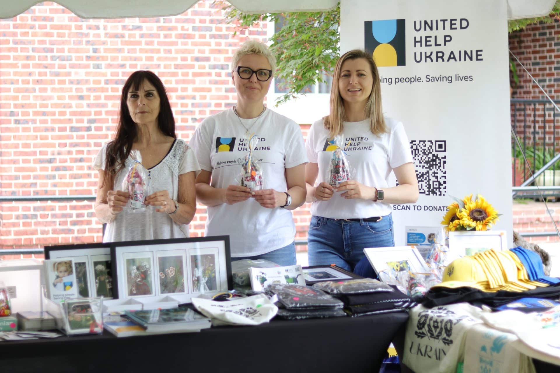 Three women with Ukrainian souvenirs in the Civilians HELP booth at the Passport DC 2025