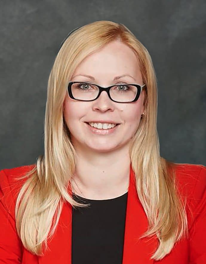 A blond-haired woman, wearing glasses in business casual outfit.