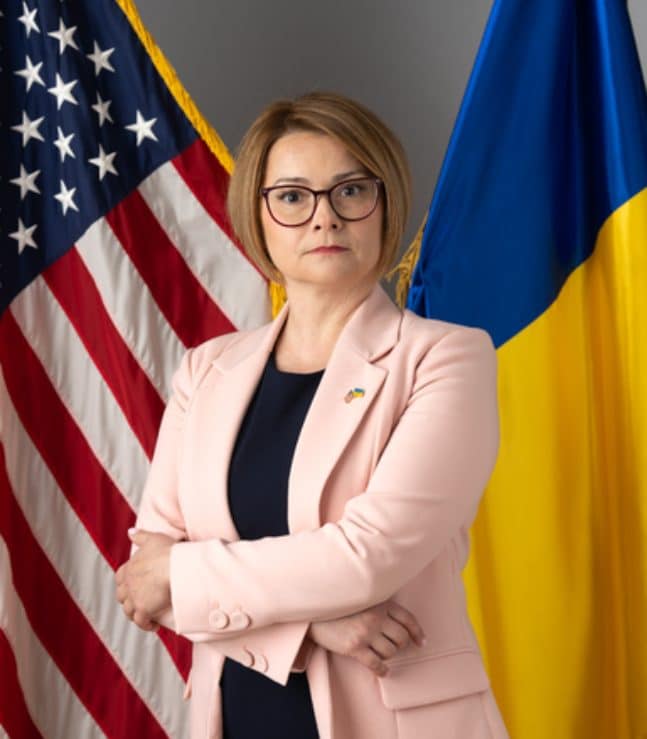 Maryna Baydyuk, President of Civilians HELP, with Ukrainian and American flags behind.